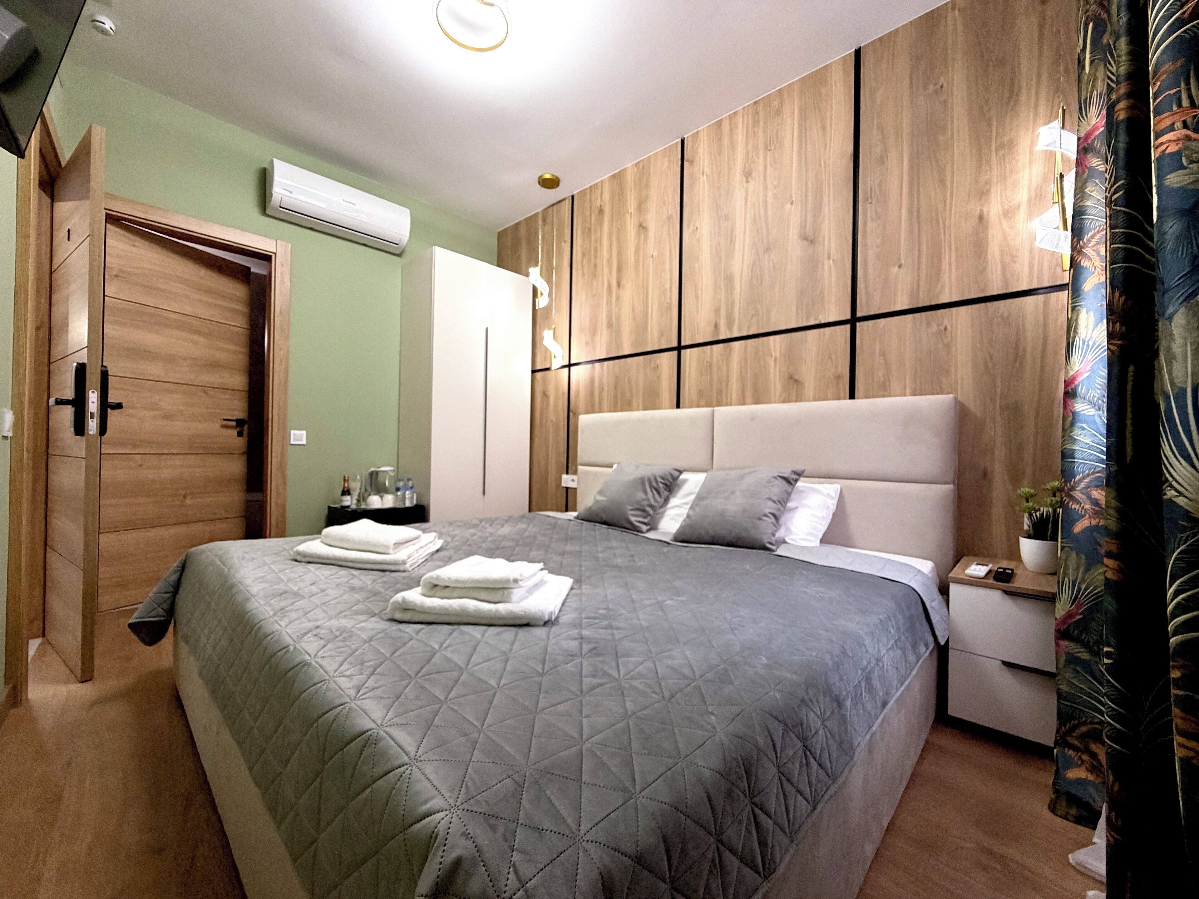 A modern bedroom with a large bed, a wooden wardrobe, a nightstand, and a potted plant.
