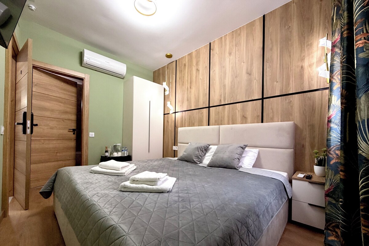 A modern bedroom with a large bed, a wooden wardrobe, a nightstand, and a potted plant.