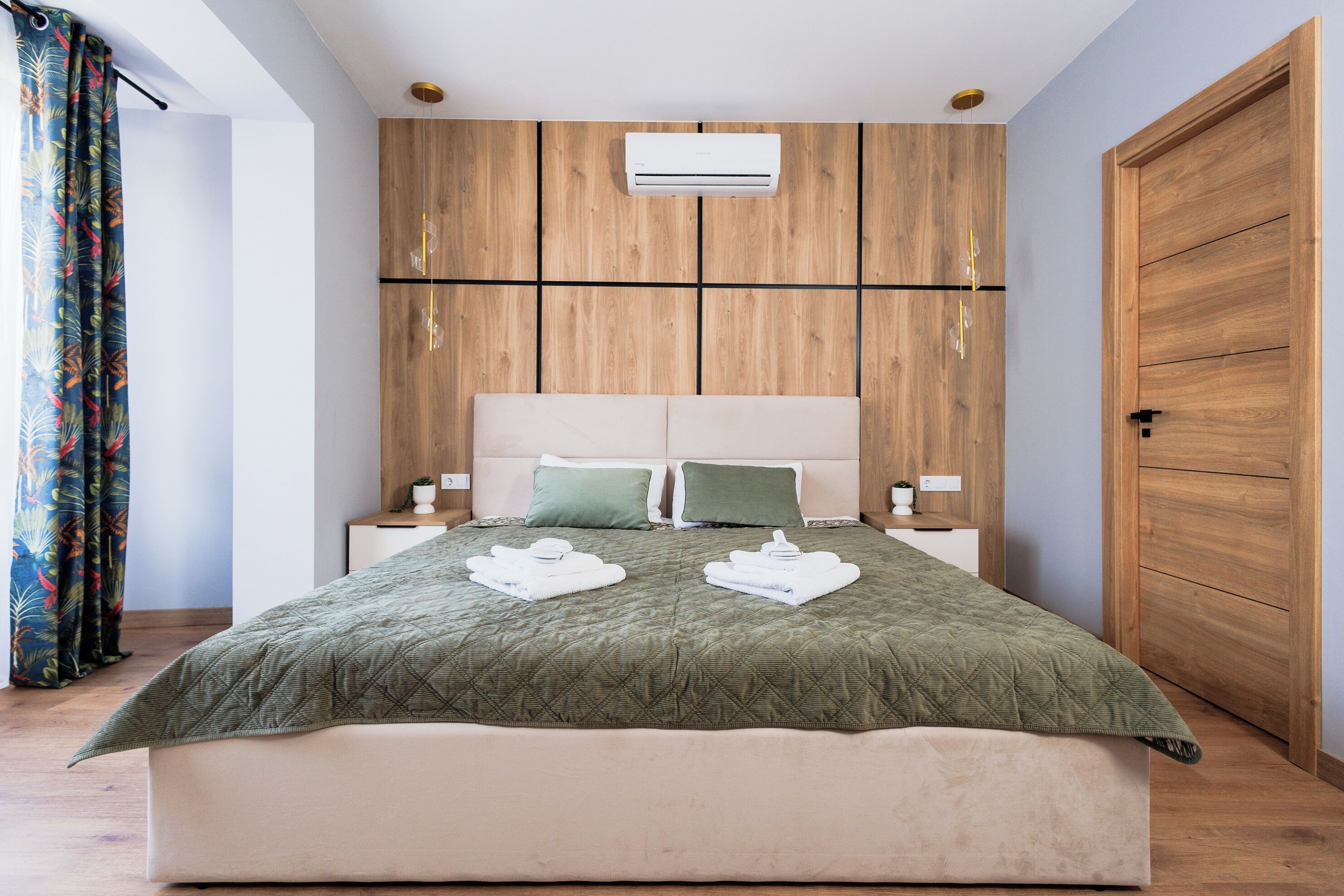 A modern bedroom with a large bed, wooden panel walls, a built-in air conditioning unit, and a nightstand with a lamp.