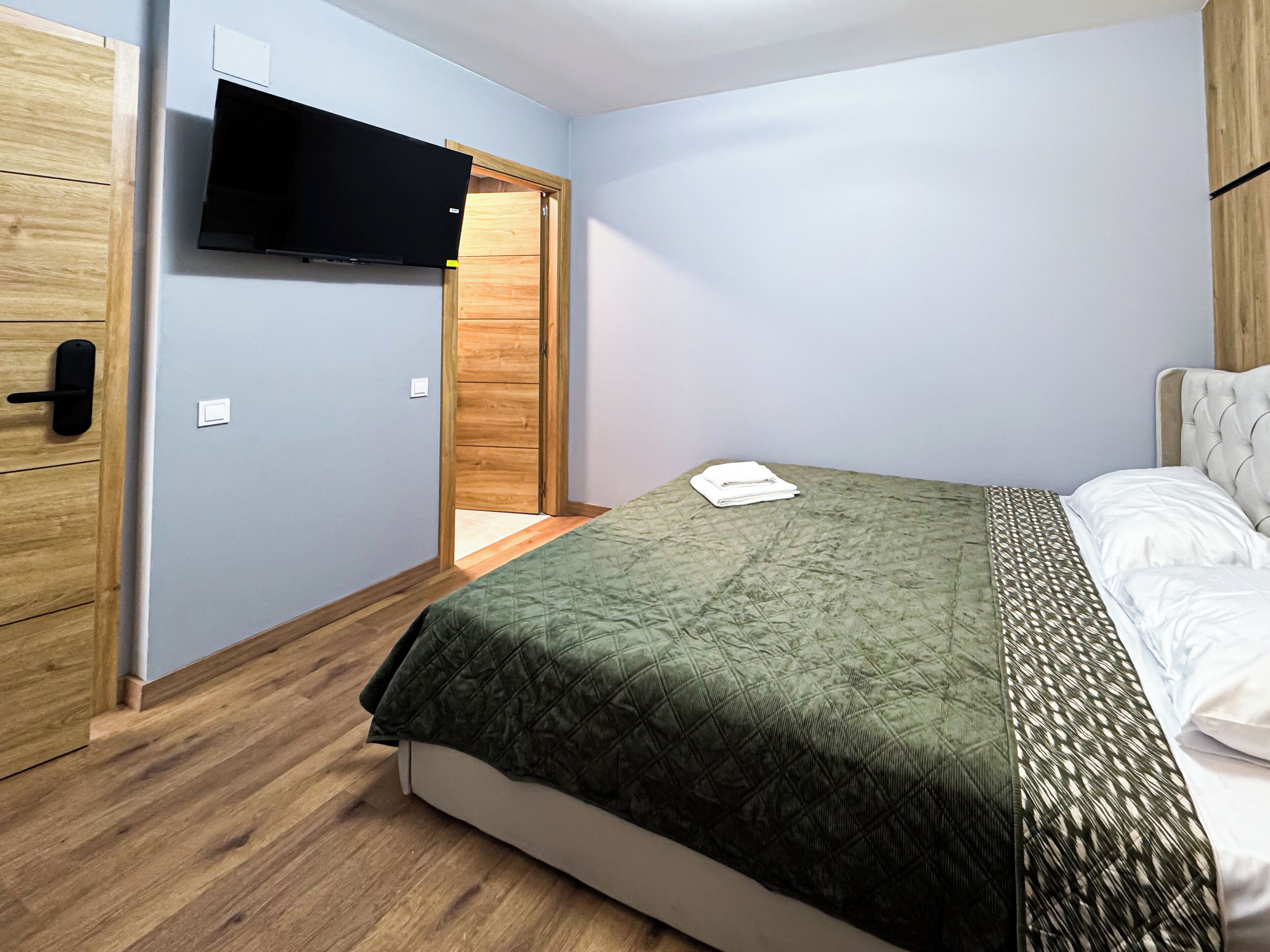 Un dormitorio con cama, televisor montado en la pared, piso de madera y armario.