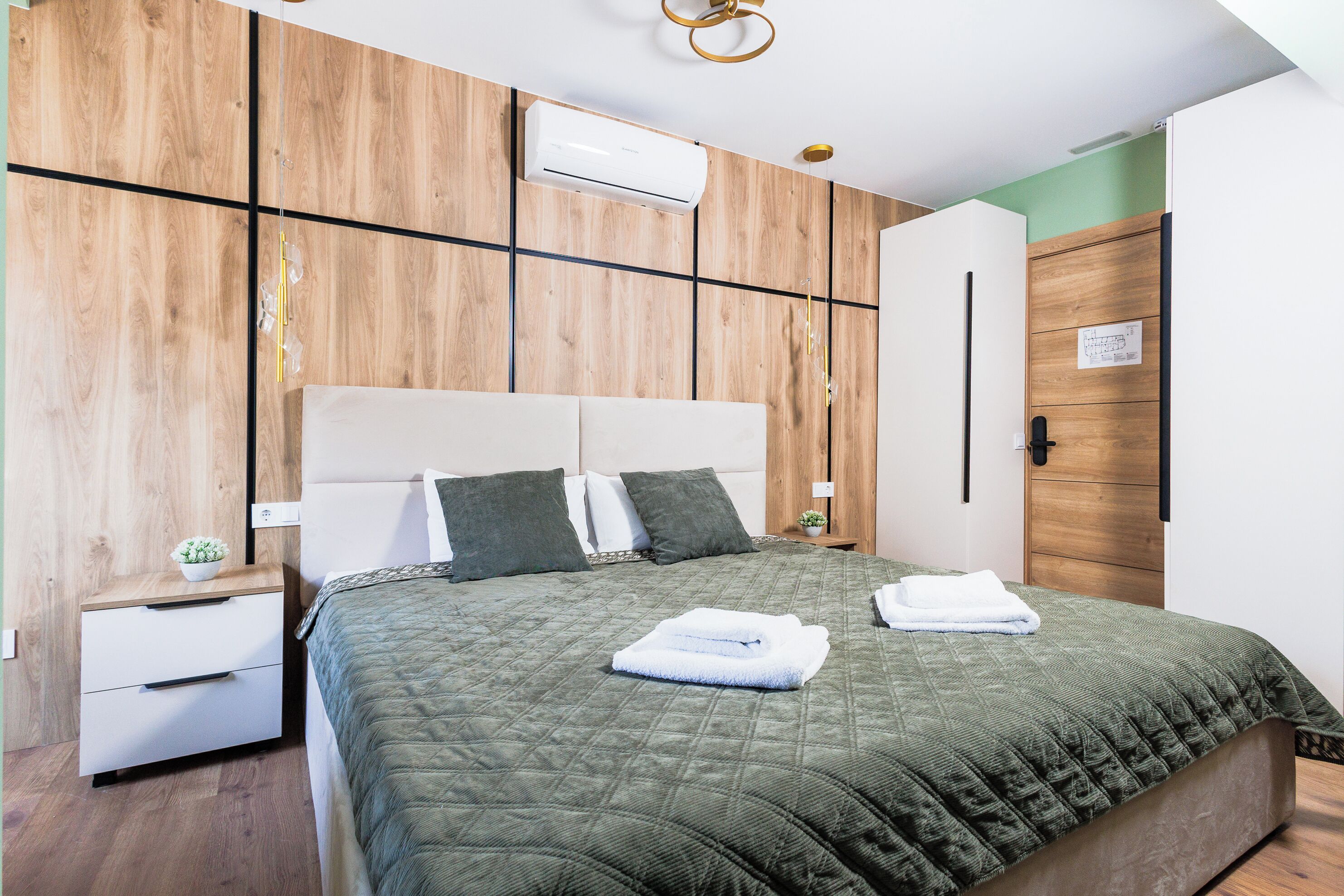 A bedroom with a bed, a nightstand, a wall-mounted air conditioner, and a wooden door.