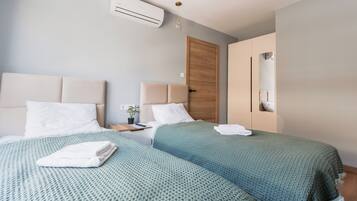 Et hotelværelse med to senge, en trædør, en klimaanlæg, et sengebord med en lampe og en lille potteplante.