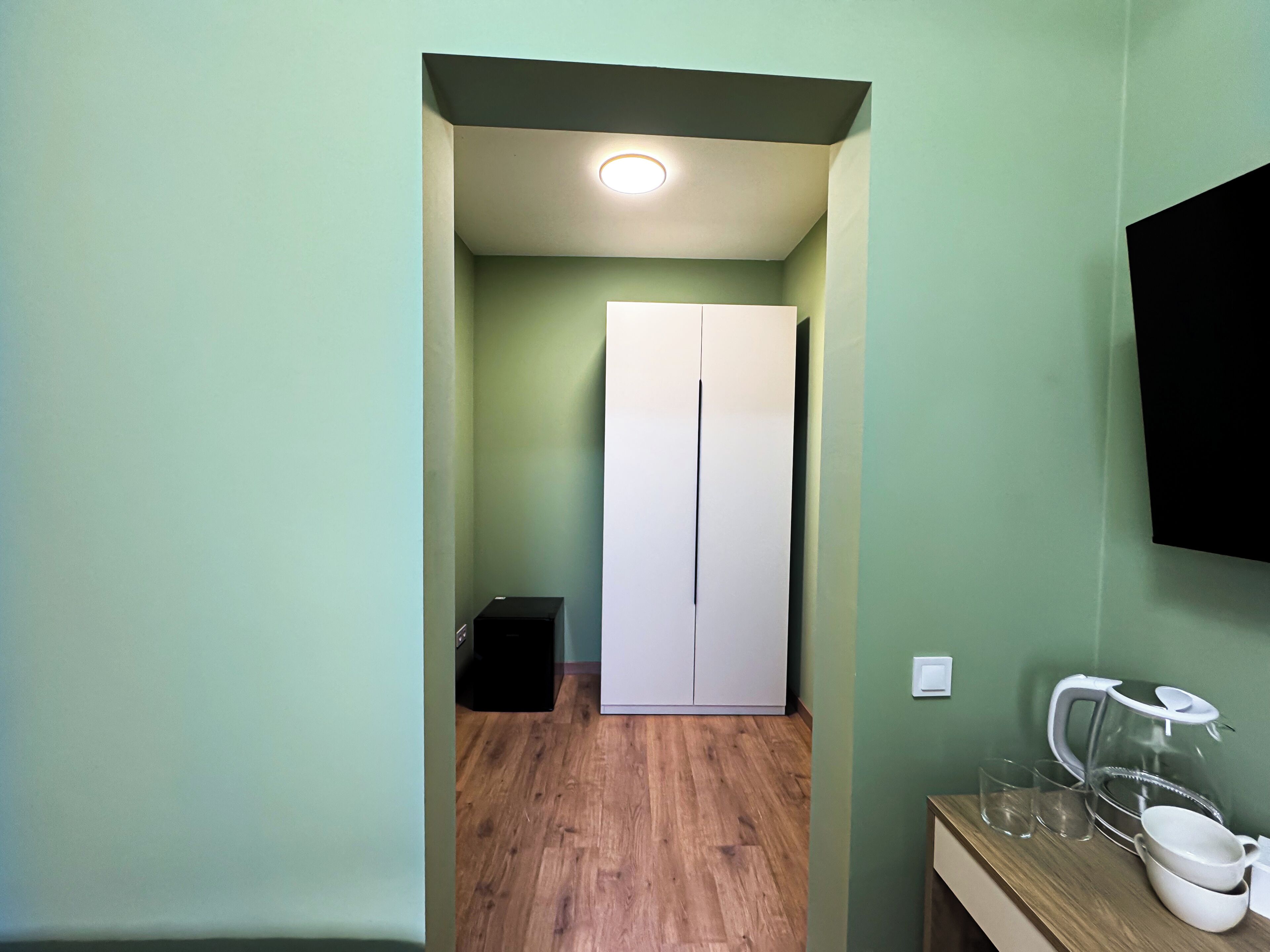 Un pasillo con suelo de madera, un armario blanco y un mueble negro pequeño.