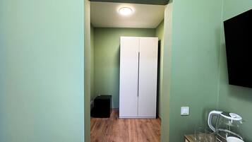 Un pasillo con suelo de madera, un armario blanco y un mueble negro pequeño.