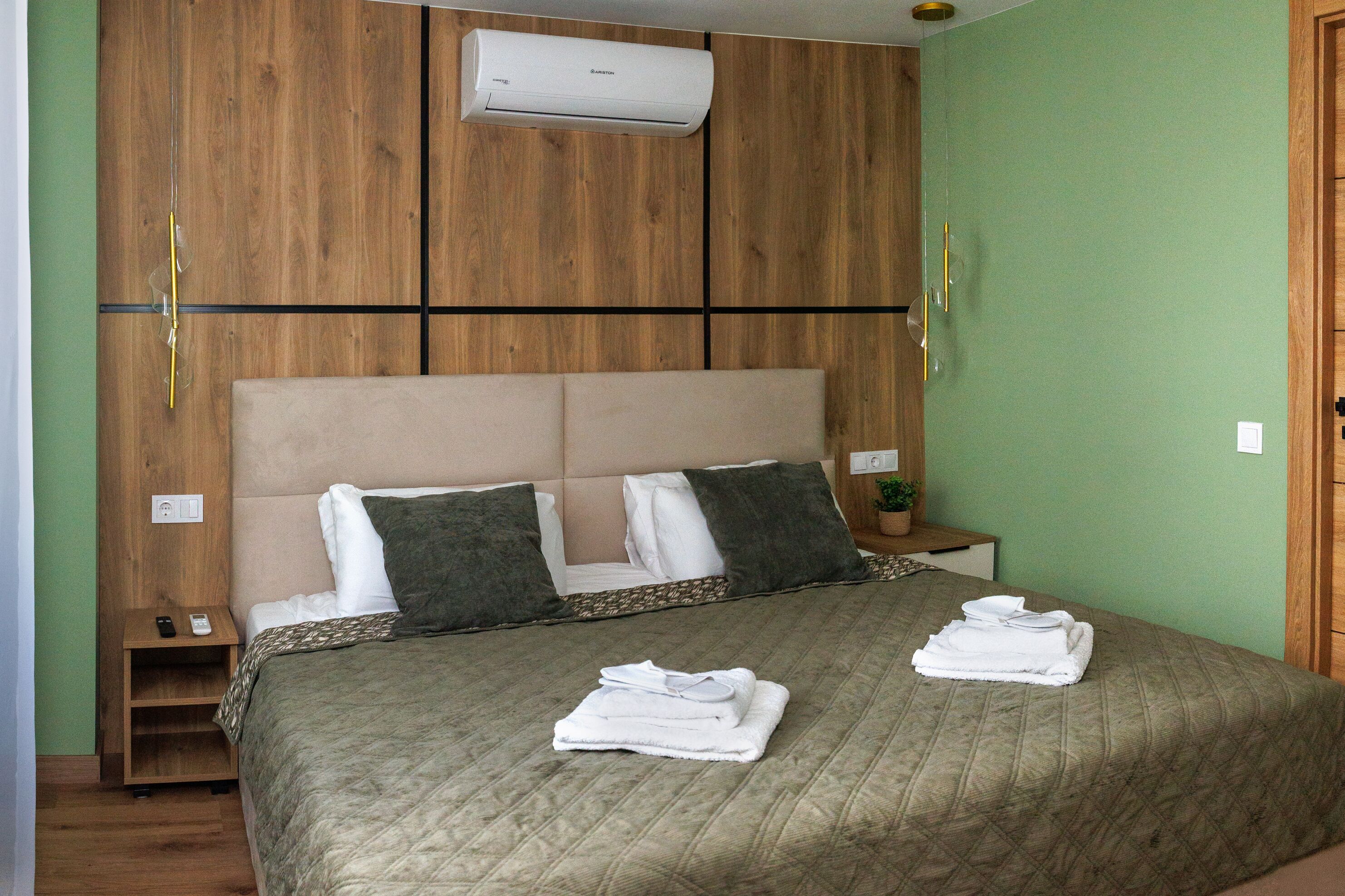 Een slaapkamer met een bed, kussens, een nachtkastje met een afstandsbediening, een wandairconditioner en een nachtkastje.