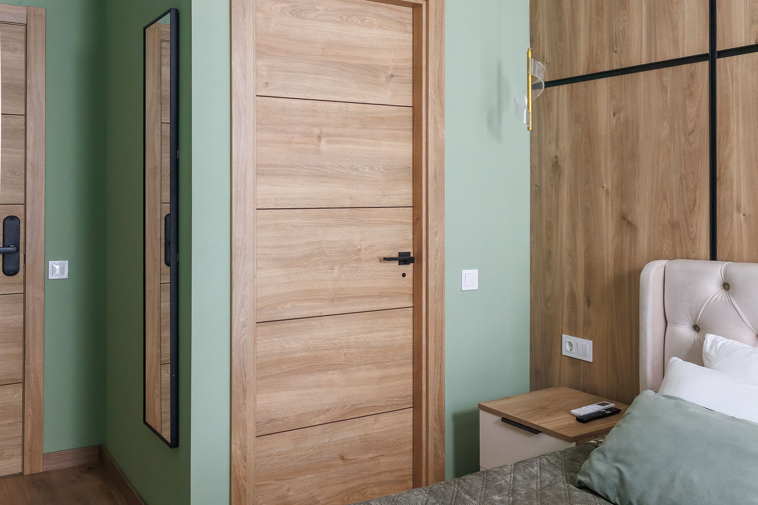 A bedroom with a bed, a nightstand, a wooden wardrobe, and a mirror.