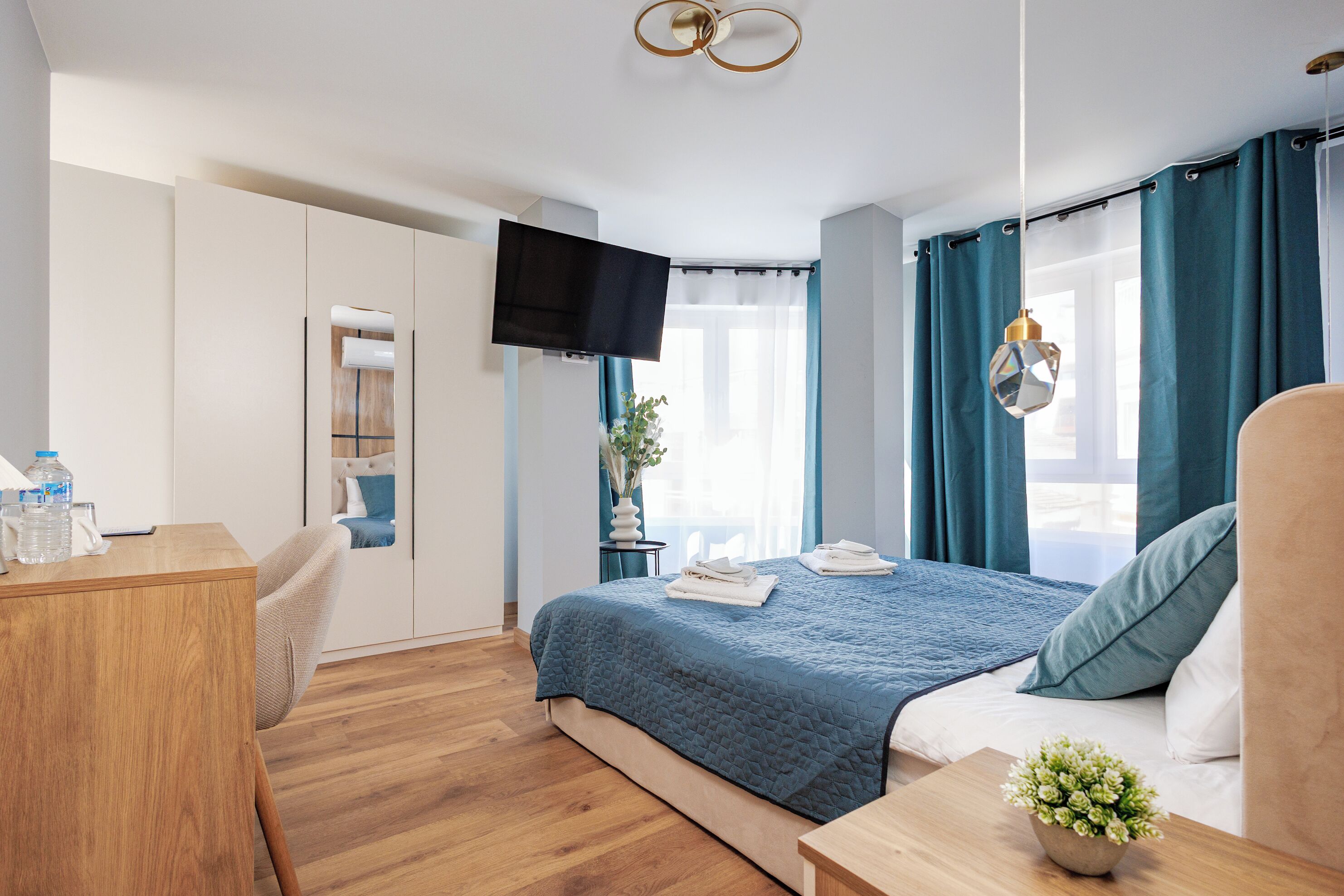 Una habitación de hotel con cama, escritorio, televisor y ventana con cortinas.