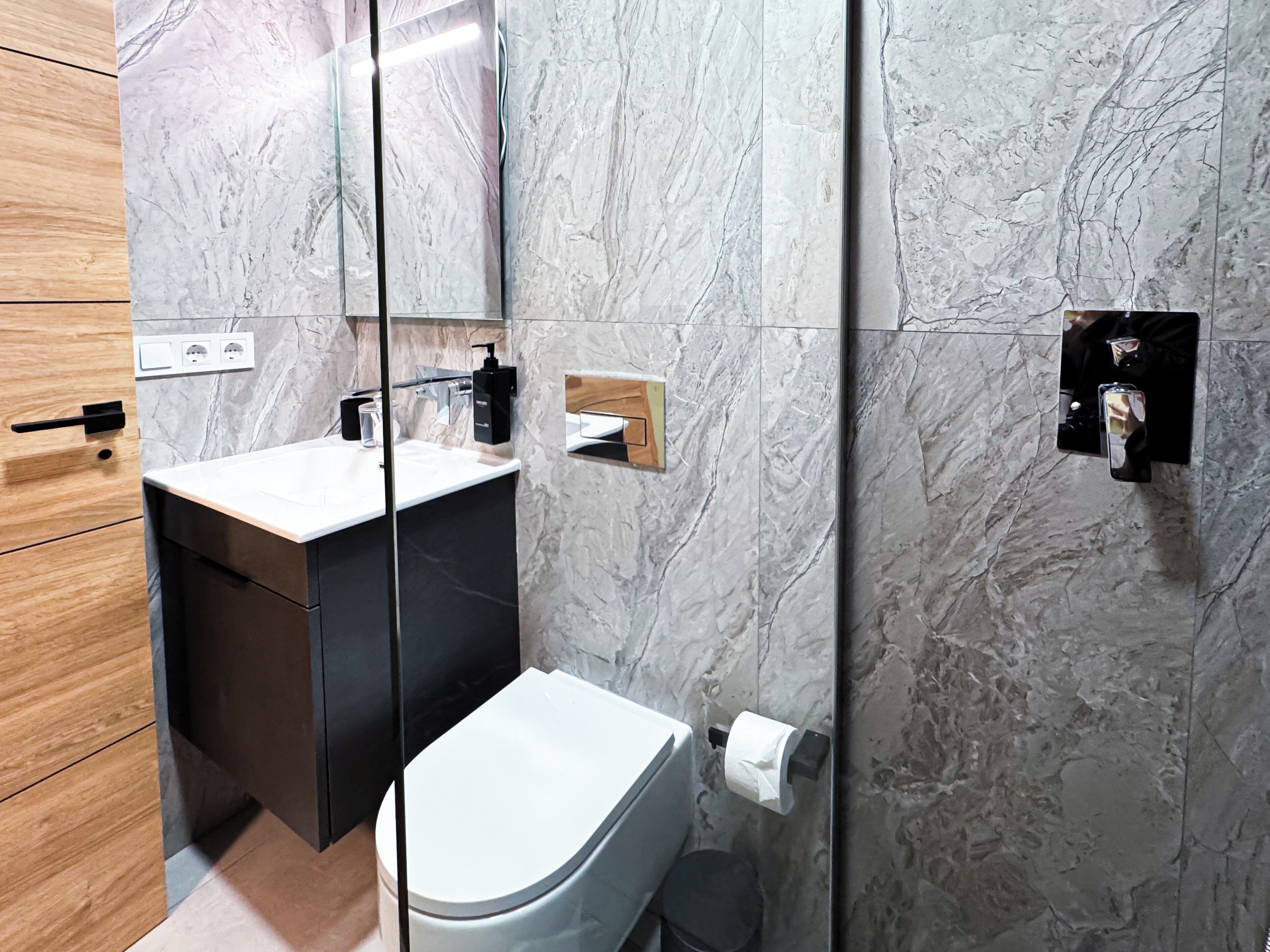 A modern bathroom with a marble backsplash, a white sink, and a black toilet.