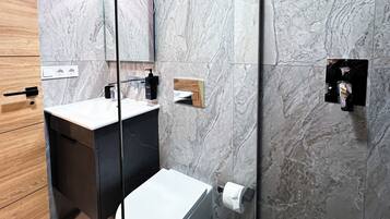A modern bathroom with a marble backsplash, a white sink, and a black toilet.