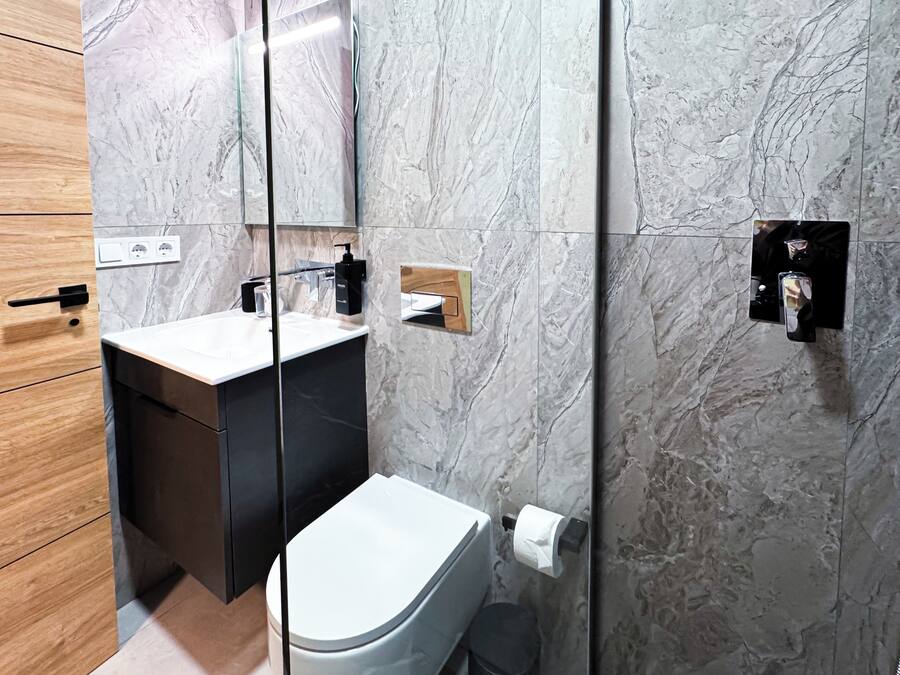 A modern bathroom with a marble backsplash, a white sink, and a black toilet.