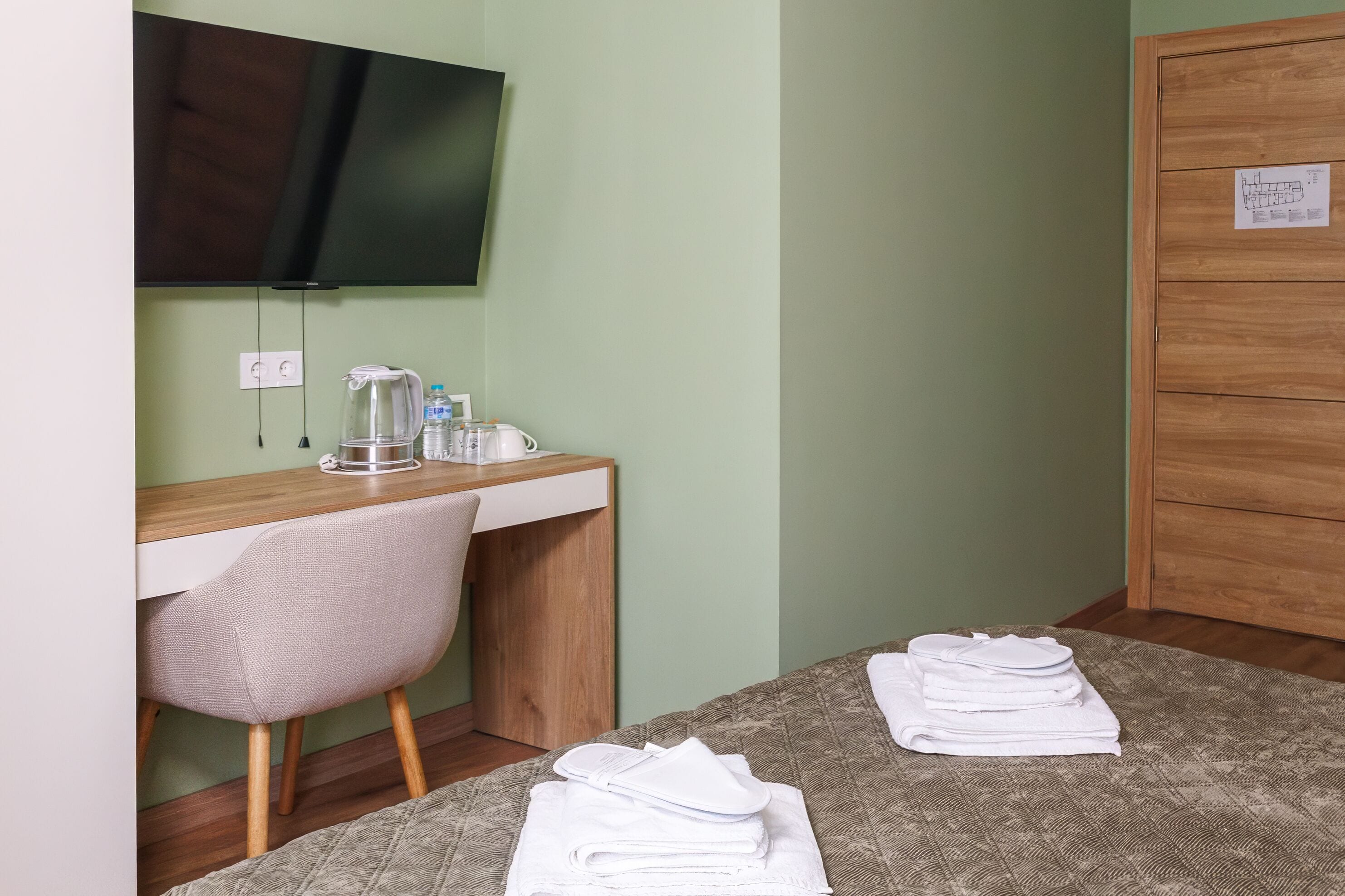 Habitació d'hotel amb un llit, escriptori amb cadira, televisió i armari de fusta.