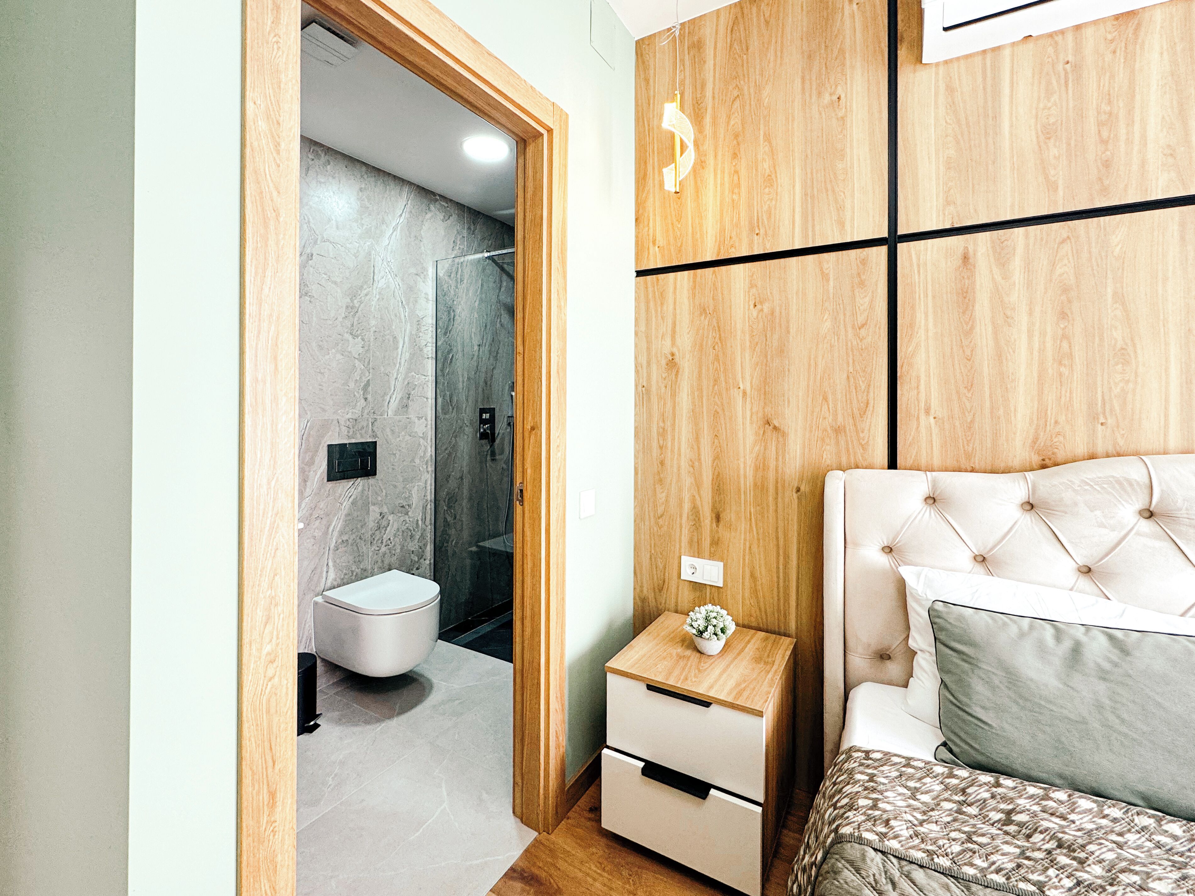 Un dormitorio moderno con cabecera de madera, mesita de noche con lámpara y colcha estampada.