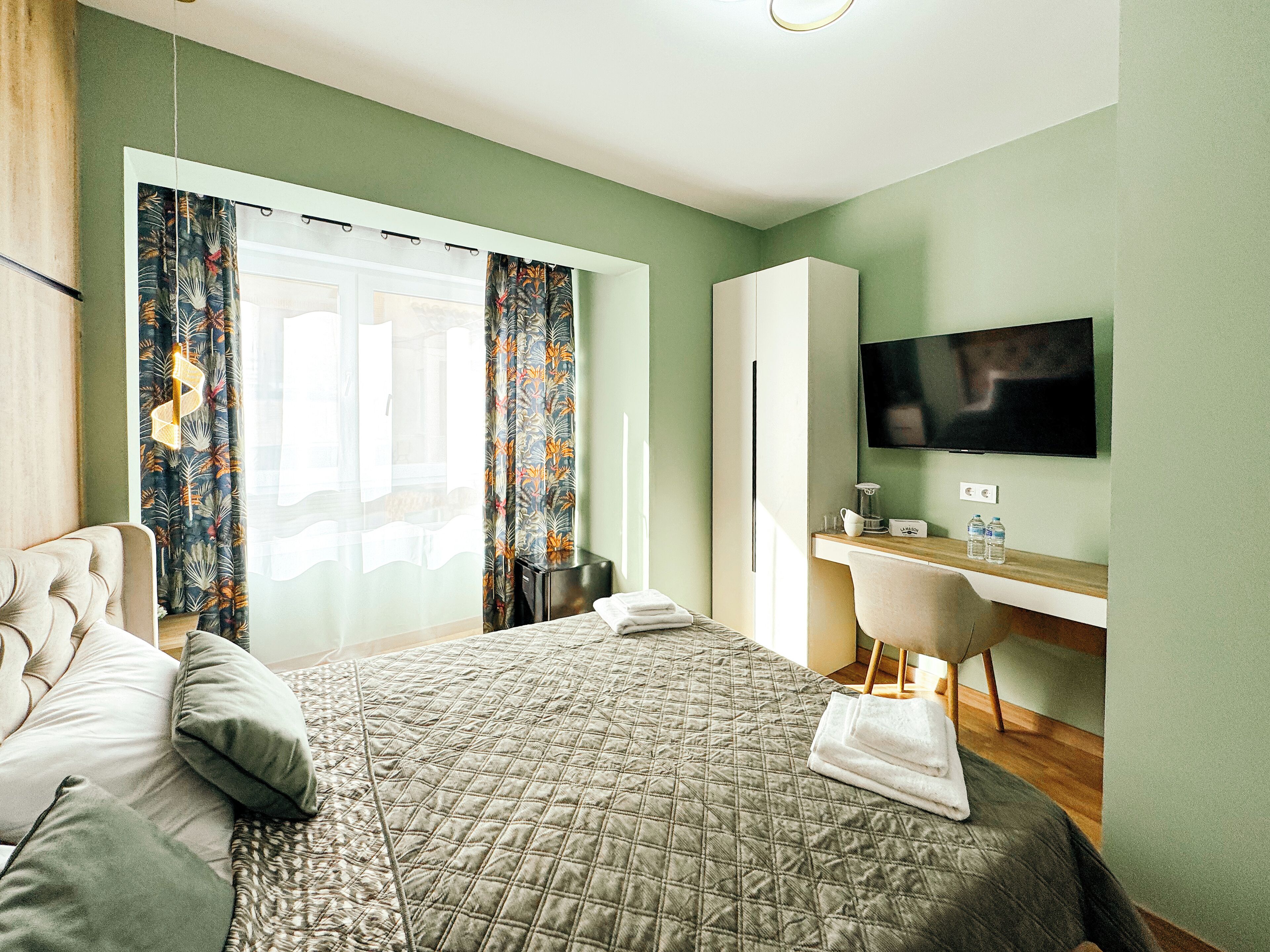 A hotel room with a bed, a desk, a chair, a TV, and a window with curtains.