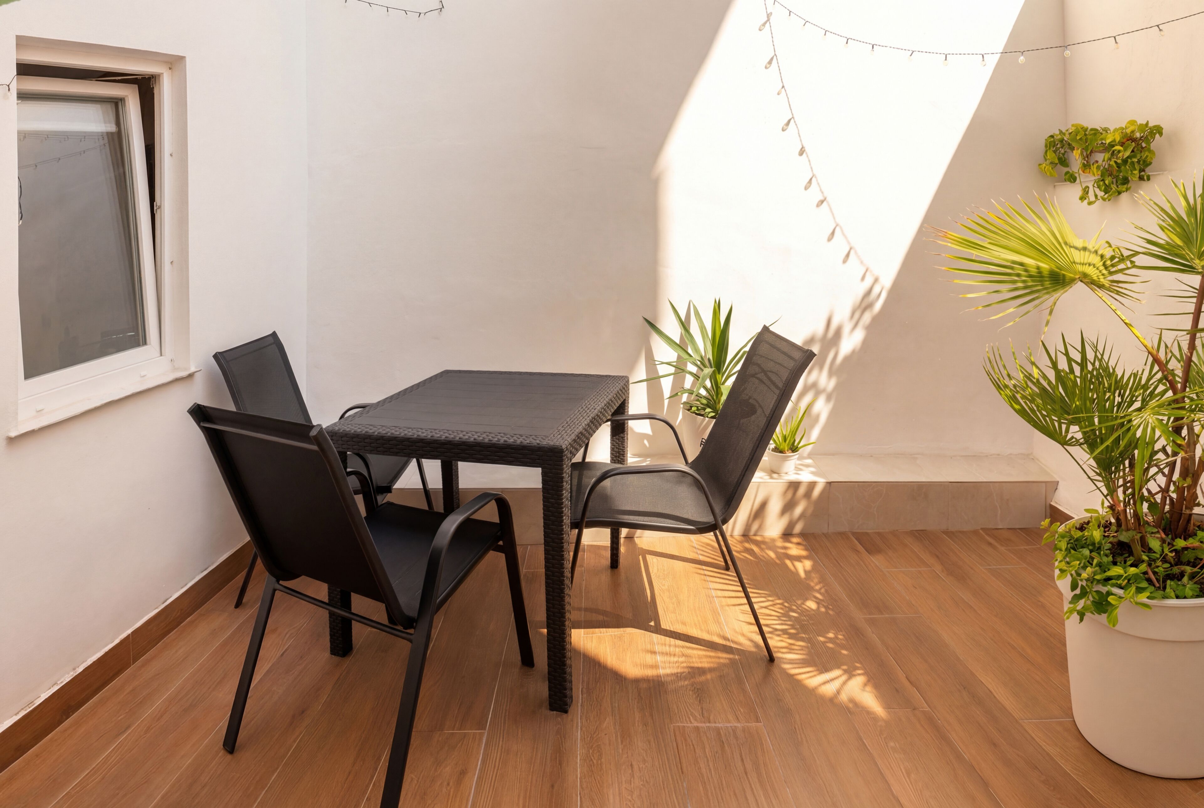 A small patio with a table and chairs, potted plants, and a window.