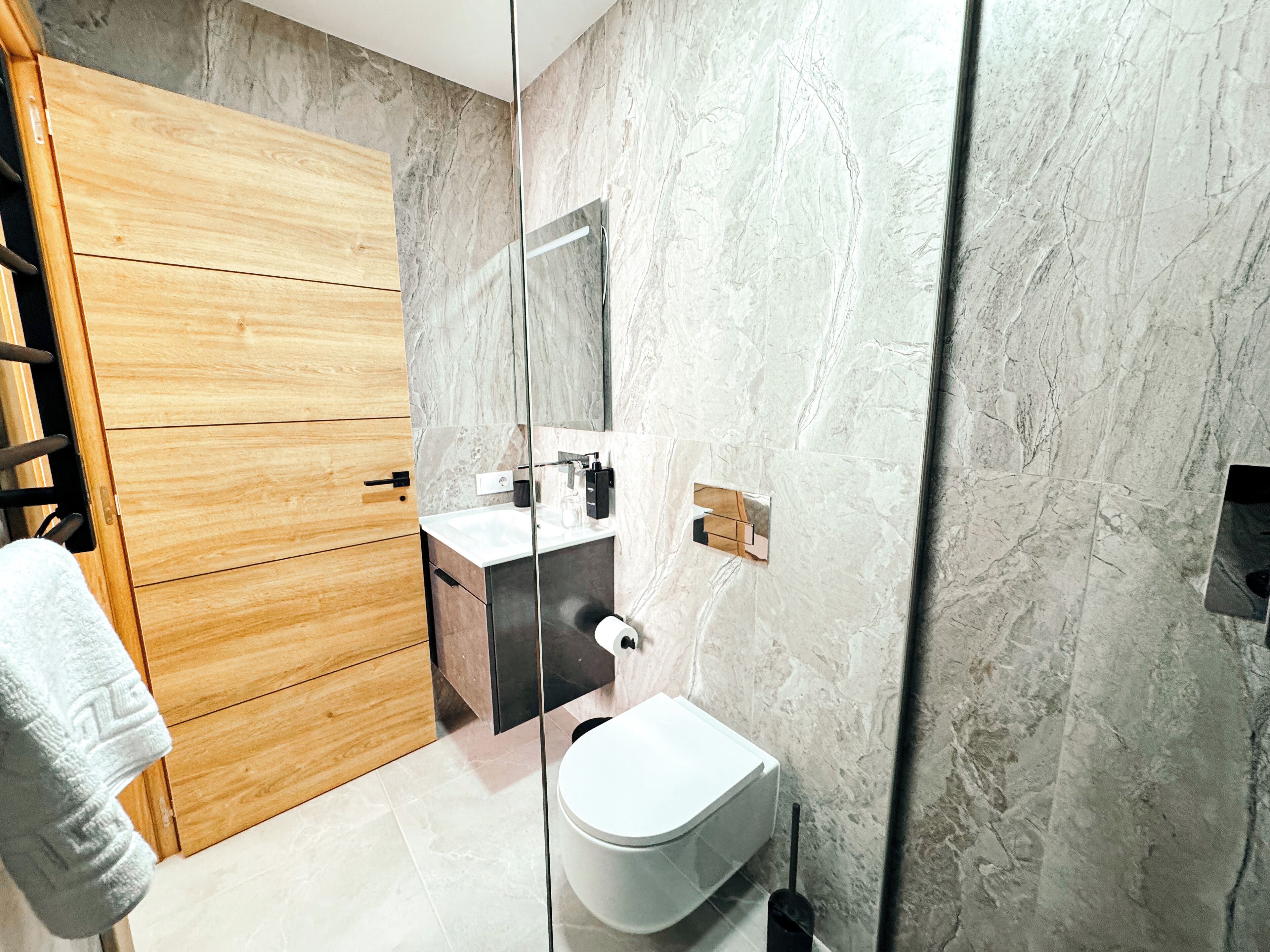 Un baño moderno con tocador de madera, inodoro blanco y salpicadero de mármol.