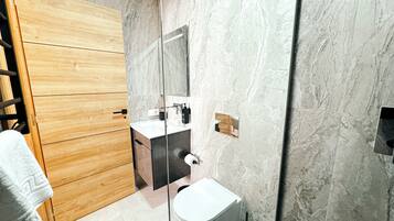 Un baño moderno con tocador de madera, inodoro blanco y salpicadero de mármol.
