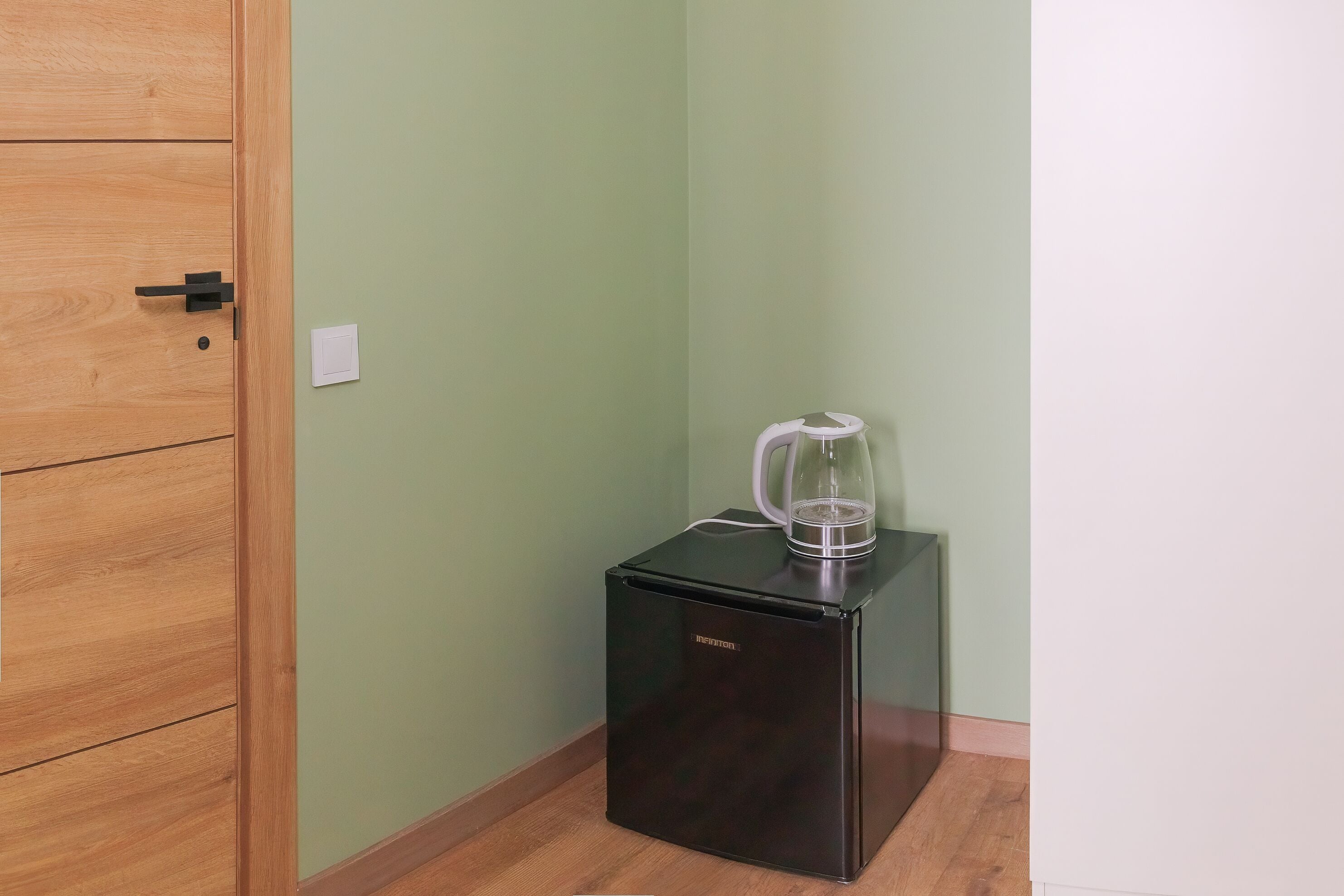 Ein schmaler Raum mit einem Holzschrank, einem kleinen schwarzen Gerät und einem weißen Tisch mit einem Glasbehälter.