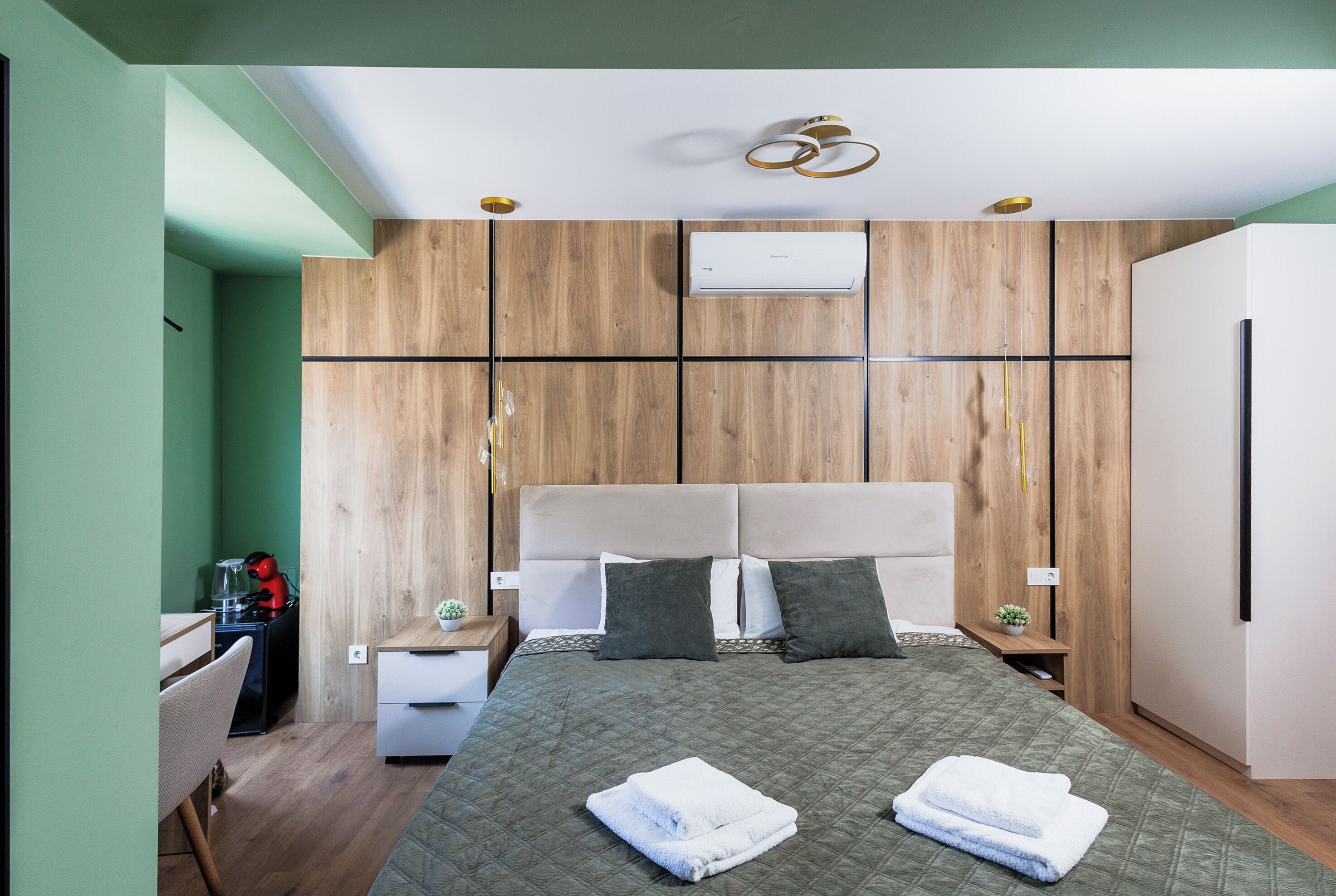 A modern bedroom with a large bed, wooden panel walls, a built-in air conditioner, and a small desk with a chair.