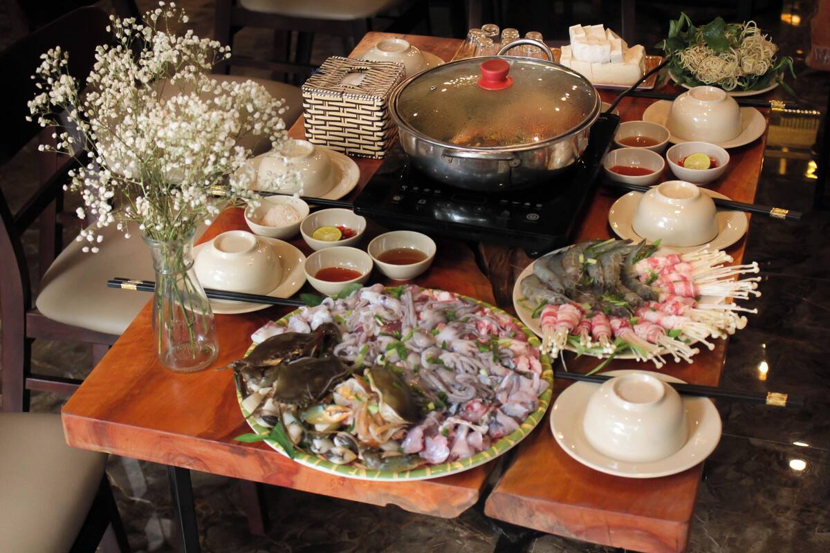 Una mesa de comedor con diversos platos, incluyendo mariscos y un recipiente con comida caliente, junto con varios cuencos y un jarrón de flores.