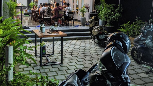 Een restaurant met een neonreclame, terras en potplanten.