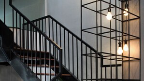 Een trap met houten treden en zwarte leuningen, een potplant en hangende lampen.