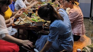 Een groep mensen dineert aan een tafel in een modern restaurant met een bakstenen muur en industriële verlichting.