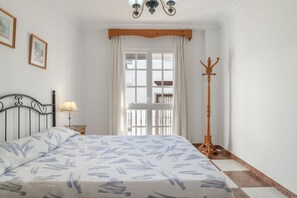 Ein Schlafzimmer mit einem Bett, einem Nachttisch, einer Lampe, einem Kleiderständer und einem Fenster mit Vorhängen.