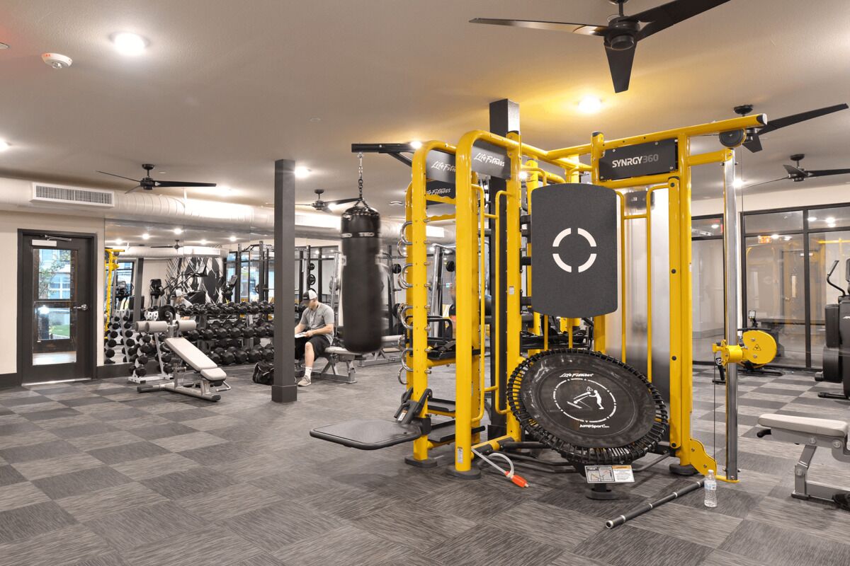A gym with various exercise equipment, including a yellow Smith machine and a punching bag.