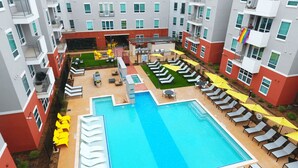 Un espace piscine aménagé sur le toit, doté de plusieurs chaises longues et de parasols, et entouré d’immeubles d’habitation.