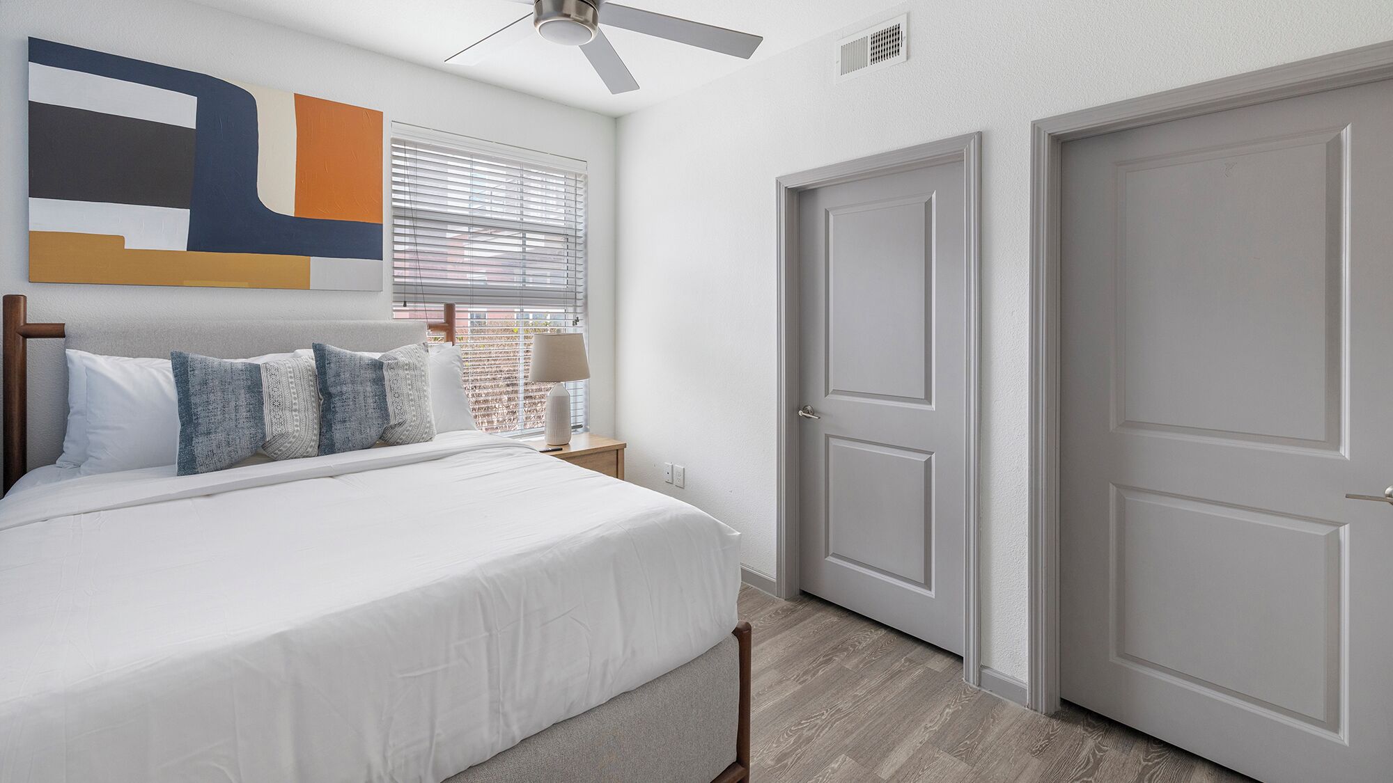 A bedroom with a bed, a nightstand, a lamp, a ceiling fan, and two doors.