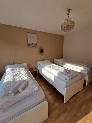 Ein Hotelzimmer mit drei Einzelbetten, einer Kristallleuchtre, einer Wanduhr und einem gerahmten Bild.