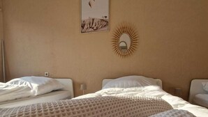 Ein Hotelzimmer mit zwei Betten, jedes mit einer gemusterten, beige farbenen Decke und weißen Kissen. An der Wand befindet sich ein Spiegel mit Sonnendesign und ein gerahmtes Bild darüber.