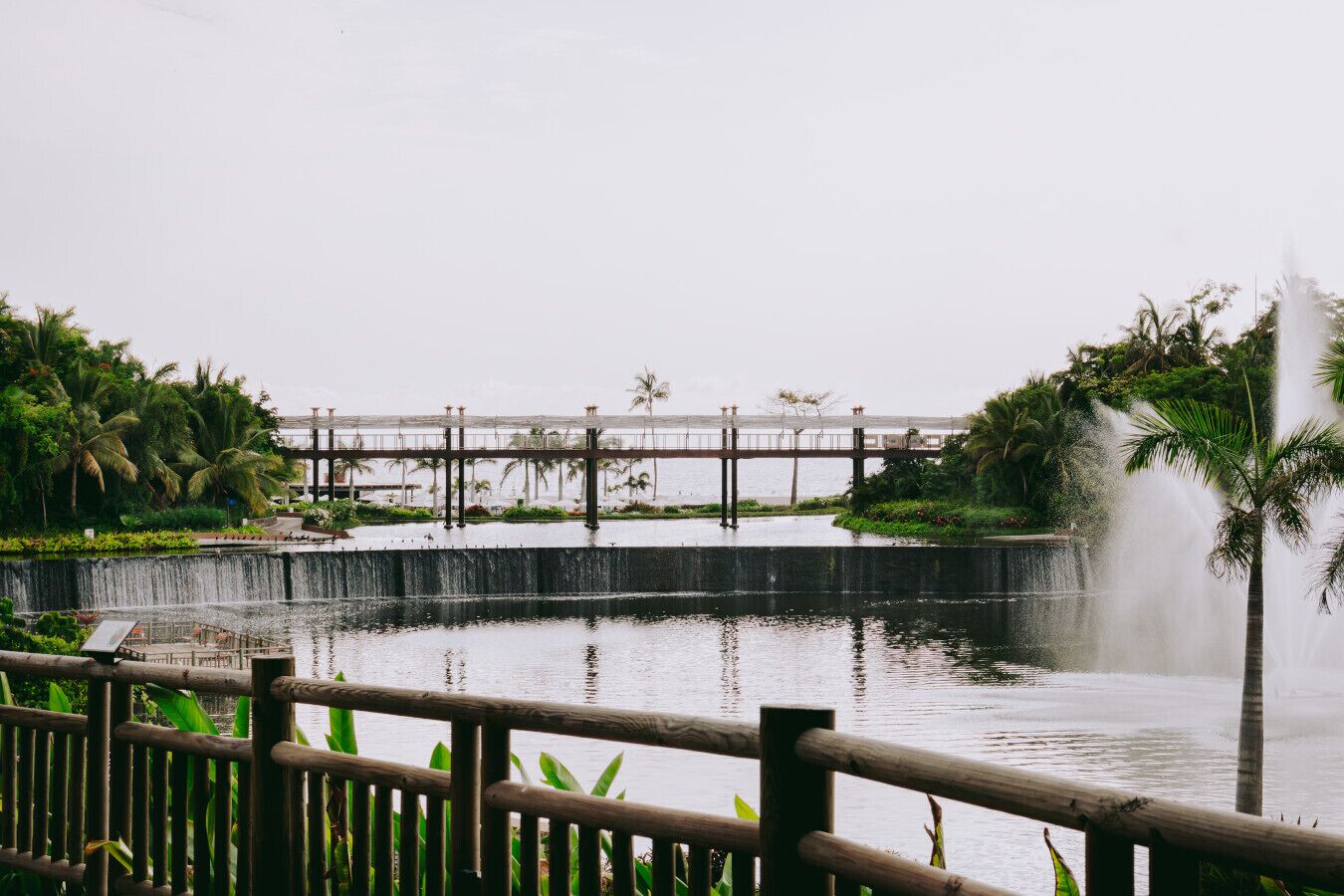 A waterfront view with a wooden fence, a bridge, and a fountain.