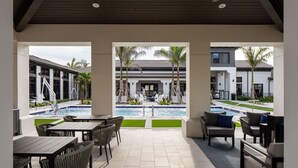 Un espacio exterior techado con piscina, asientos y vistas a un edificio con tejado de azulejos.