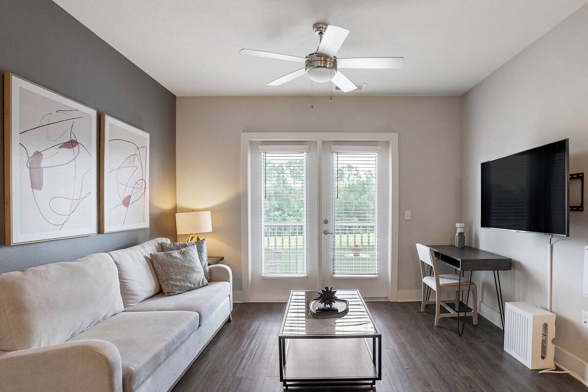 A modern living room with a sofa, coffee table, ceiling fan, and a TV mounted on the wall.