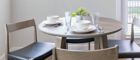Una mesa redonda de comedor con cuatro sillas, platos, tazones, vasos y cubiertos blancos.