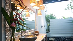 A bathroom with a wooden vanity, a large mirror, and a stone basin. There are wicker lampshades and a plant on the vanity. - SPV 8008 · LUXURY JIMBARAN VILLA BY THE BEACH (Bali)