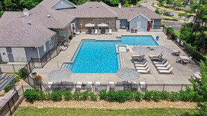 A residential property with a large rectangular swimming pool, multiple lounge chairs, and umbrellas. - Landing Apartments Charlotte - Mallard Creek (Charlotte)