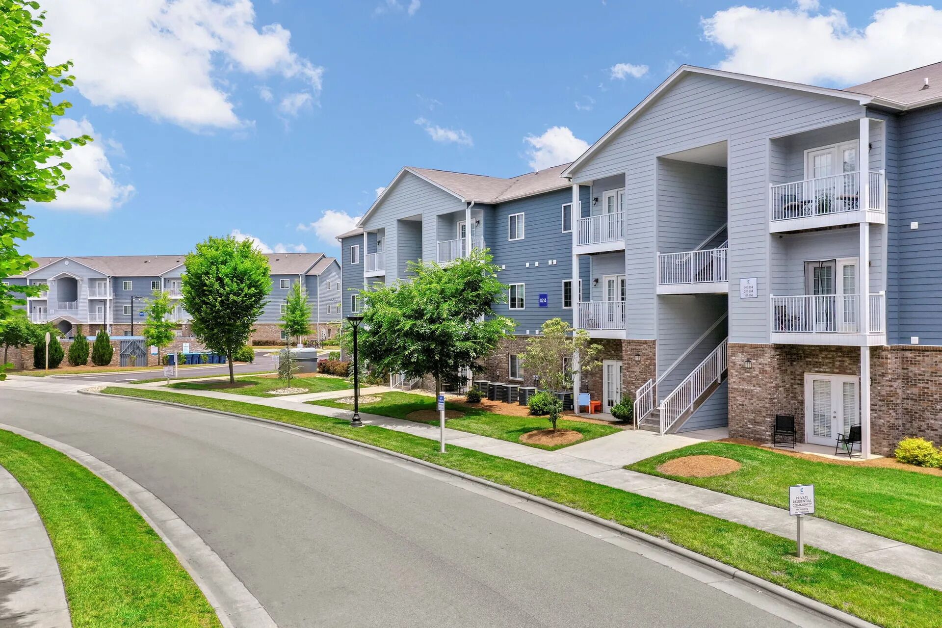 A row of two-story residential buildings with balconies, a clear sky, and a well-maintained lawn.