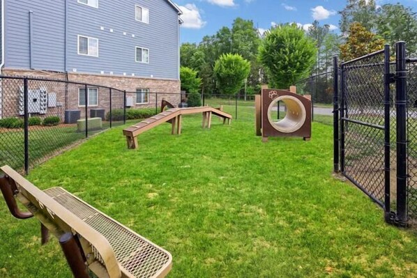 A fenced outdoor area with a wooden bench, a slide, and a circular climbing structure.