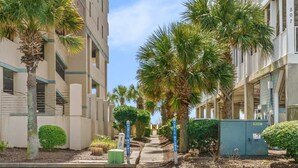 A residential street with palm trees, a sidewalk, and a utility box. - Sunny Studio Near the Beach at Palm Court (#1) (North Myrtle Beach)