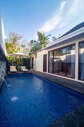 A swimming pool with two lounge chairs and an umbrella, surrounded by a white building with large glass doors. - MariJo Villa·2BR Private Pool mins to Central Ubud (Bali)