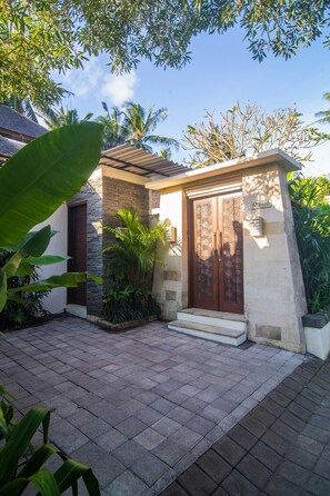 A house with a stone facade, a wooden door with intricate designs, and a small garden area with potted plants and a palm tree. - MariJo Villa·2BR Private Pool mins to Central Ubud (Bali)