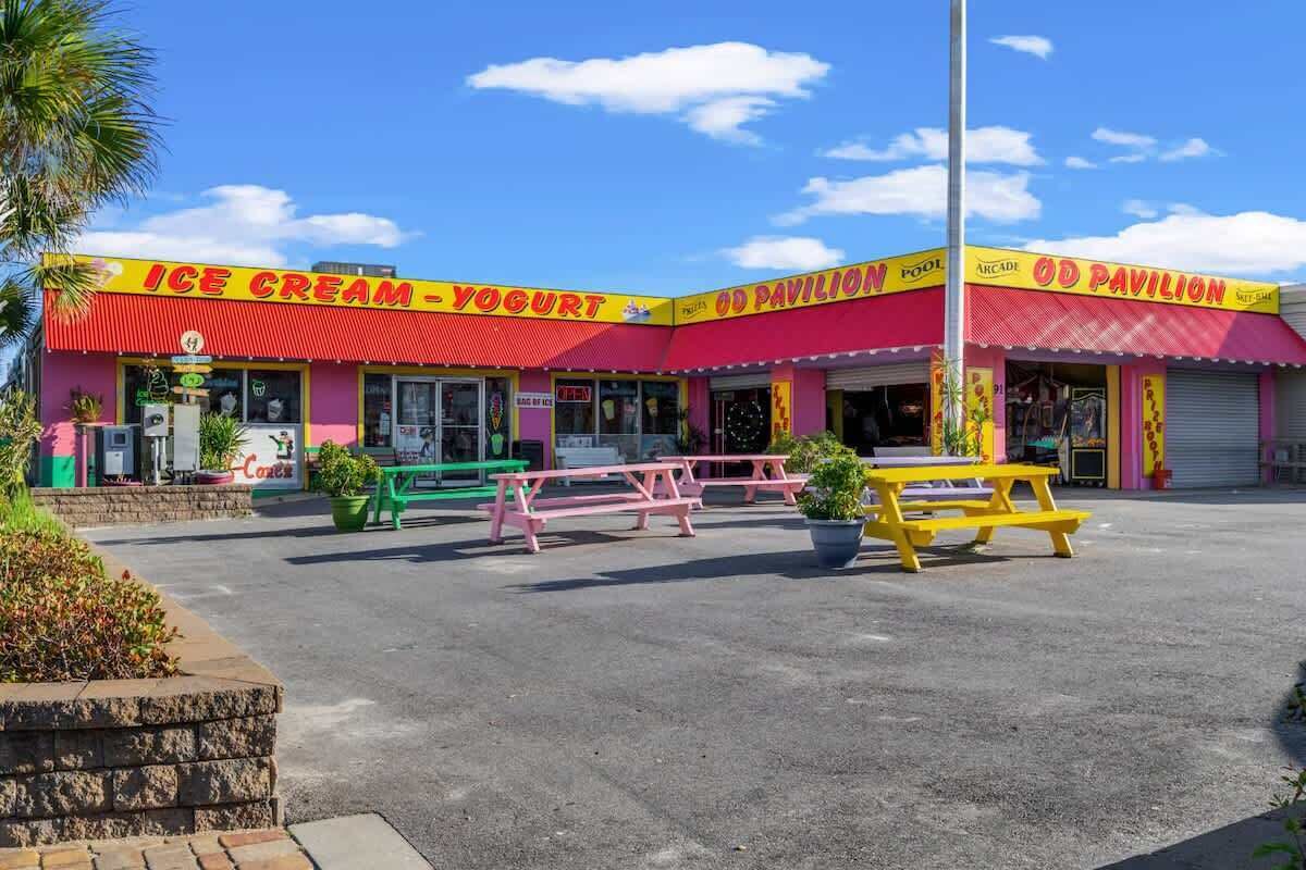 A colorful ice cream and yogurt shop with a red and yellow facade, outdoor seating, and a clear blue sky.