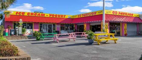A colorful ice cream and yogurt shop with a red and yellow facade, outdoor seating, and a clear blue sky.