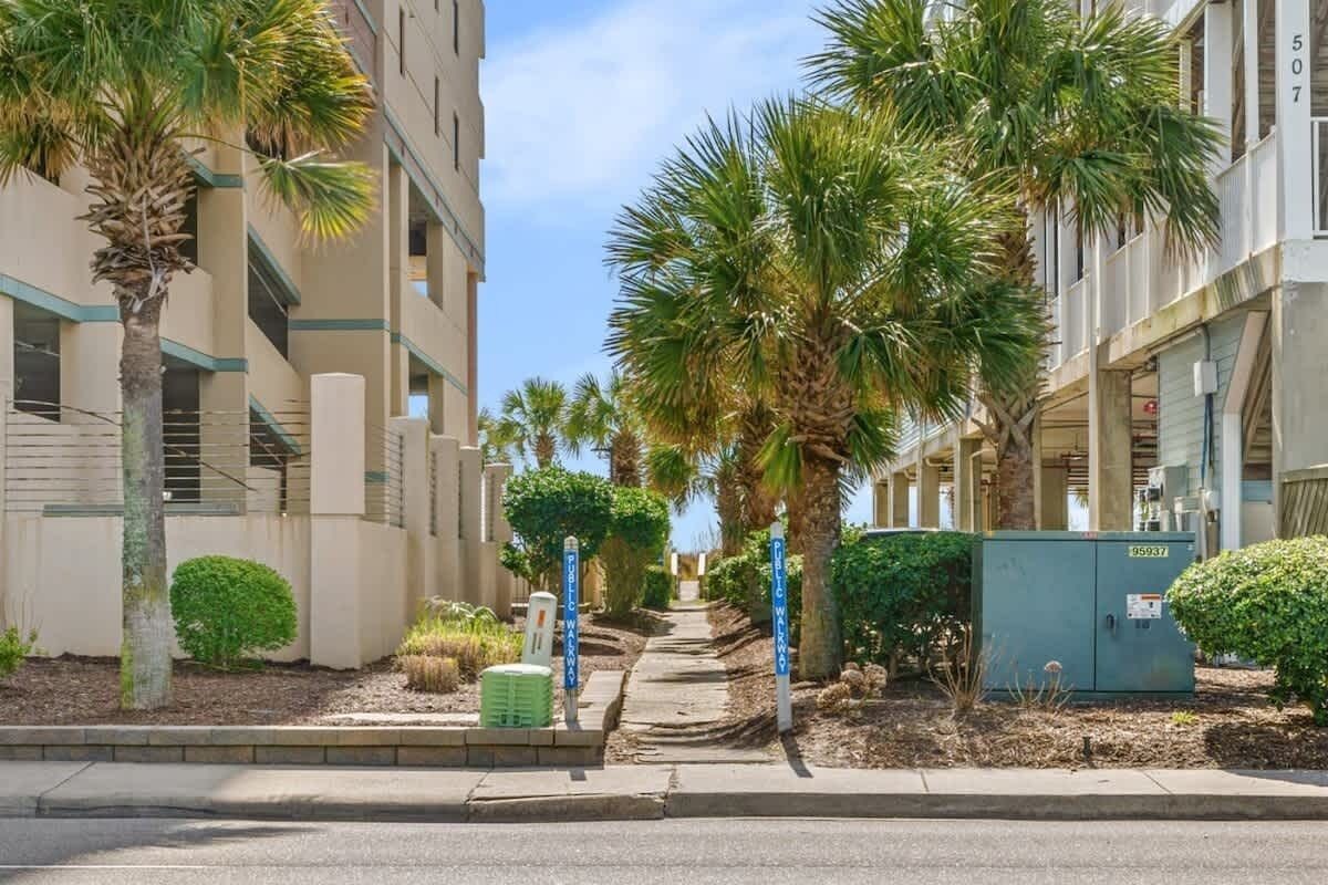A residential street with palm trees, a sidewalk, and a utility box.