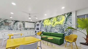 A modern kitchen with white cabinets, a yellow dining table, and a green sofa. - Sunny Studio Near the Beach at Palm Court (#12) (North Myrtle Beach)