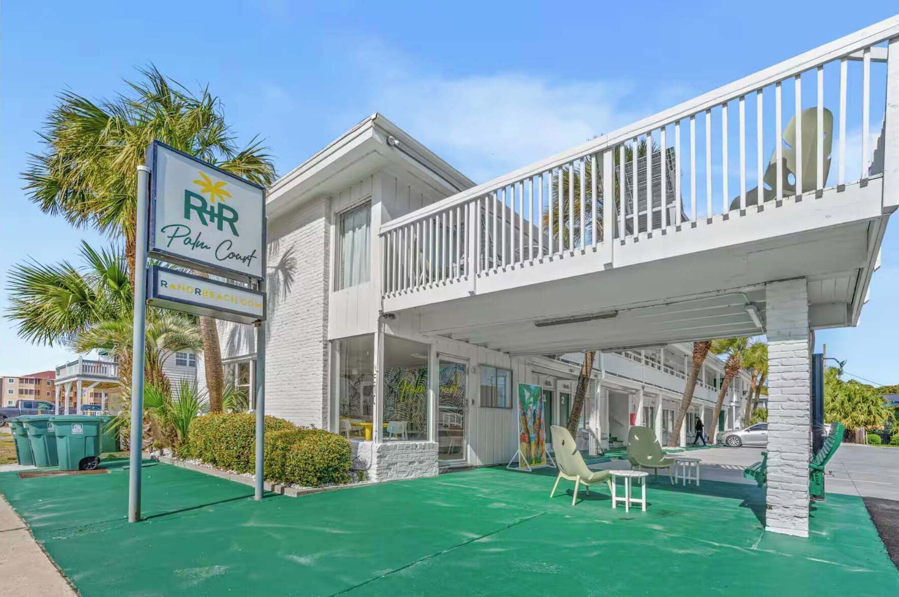 A beachfront hotel with a balcony, palm trees, and a green lawn.