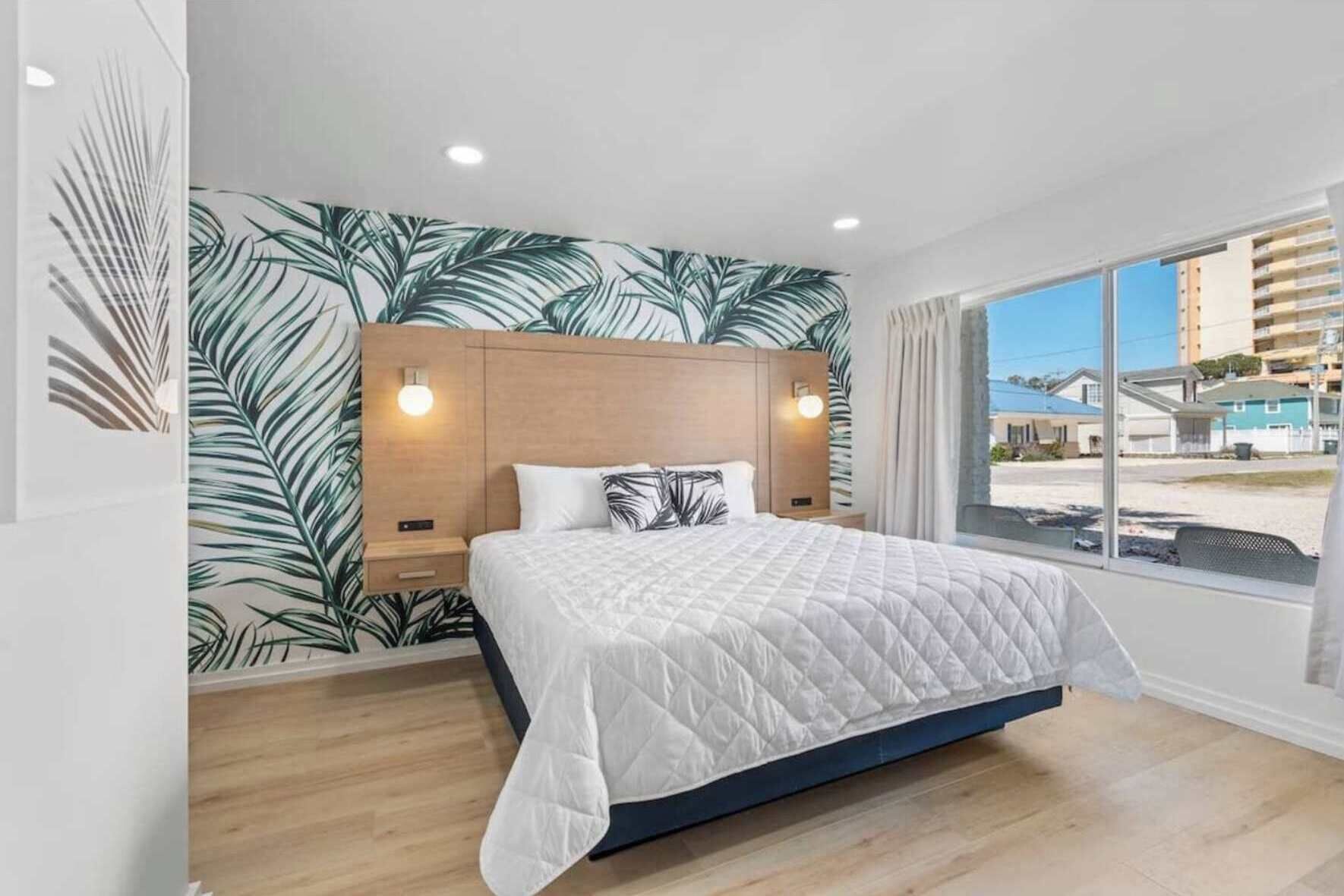 Een moderne slaapkamer met een groot bed, een houten hoofdbord en uitzicht op gebouwen door een groot raam.
