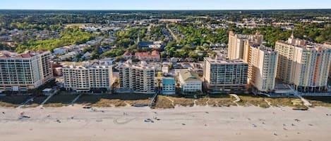 Een kuststadsgezicht met hoge gebouwen, een zandstrand en een helderblauwe lucht.